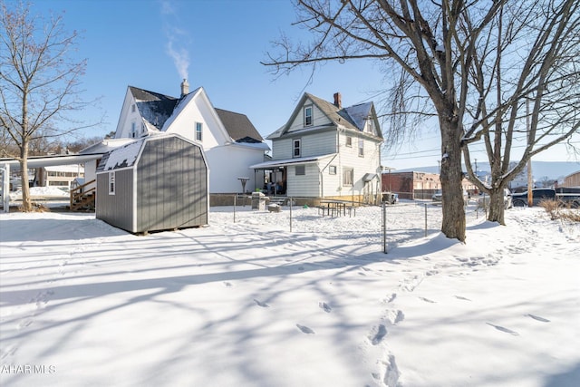 snow covered rear of property with a storage shed