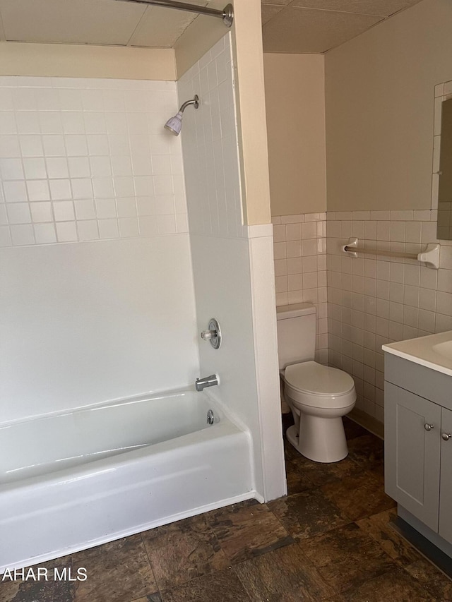 bathroom featuring toilet, stone finish flooring, shower / washtub combination, vanity, and tile walls
