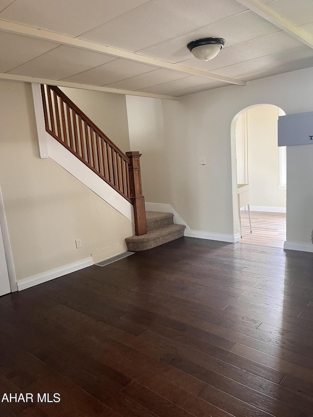 unfurnished living room featuring arched walkways, hardwood / wood-style flooring, stairs, and baseboards