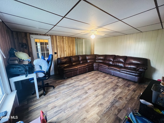 living room featuring wooden walls, hardwood / wood-style floors, ceiling fan, and a drop ceiling