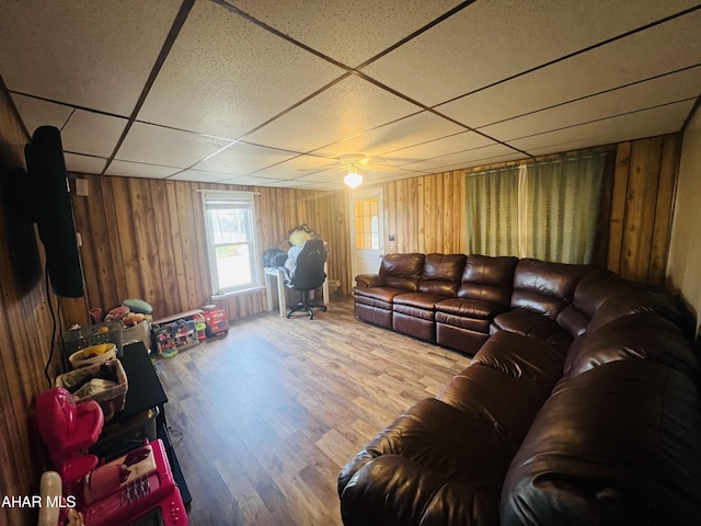 living room featuring wood walls, a drop ceiling, ceiling fan, and hardwood / wood-style flooring