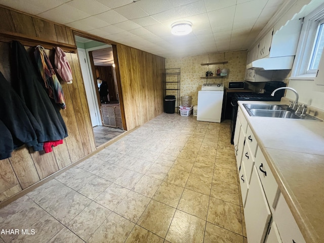 kitchen with white cabinetry, wooden walls, sink, and washer / dryer