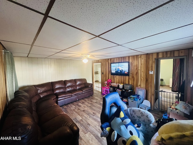 living room with wooden walls, a drop ceiling, ceiling fan, and wood-type flooring