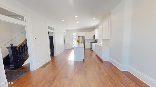 kitchen with light hardwood / wood-style flooring, appliances with stainless steel finishes, white cabinetry, a kitchen island, and a kitchen bar