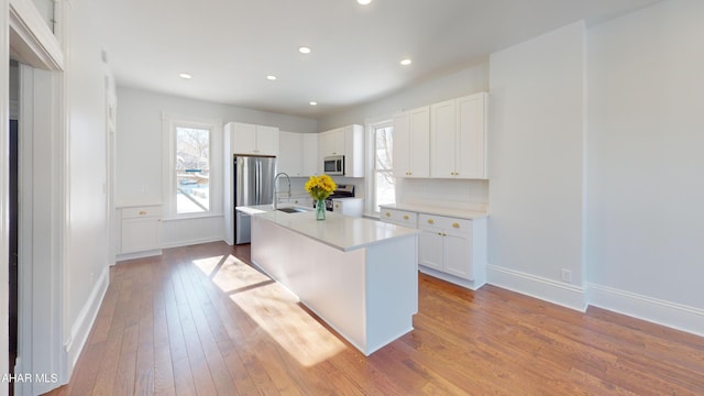 kitchen featuring sink, appliances with stainless steel finishes, an island with sink, light hardwood / wood-style floors, and white cabinets