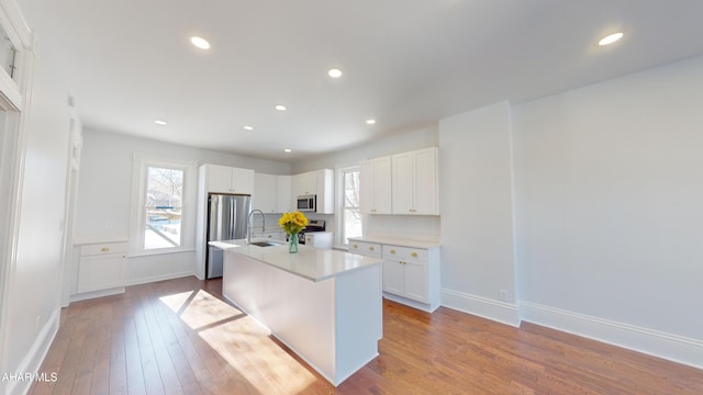 kitchen with white cabinetry, stainless steel appliances, light hardwood / wood-style floors, and a center island with sink