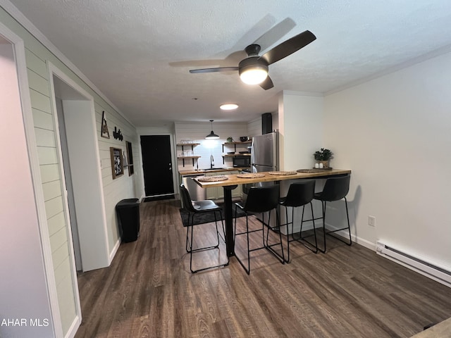 dining space featuring ceiling fan, a baseboard radiator, dark wood-type flooring, and a textured ceiling