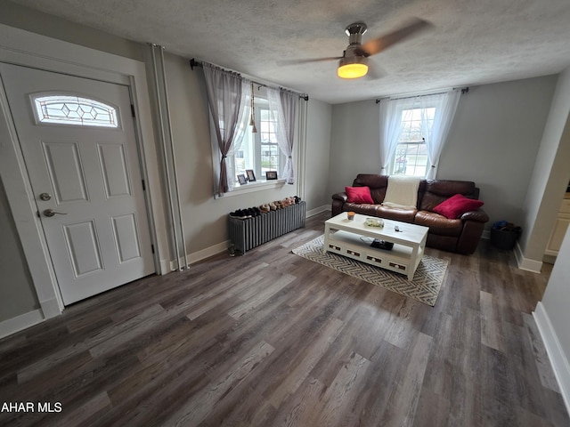 living area featuring a textured ceiling, wood finished floors, radiator heating unit, baseboards, and ceiling fan