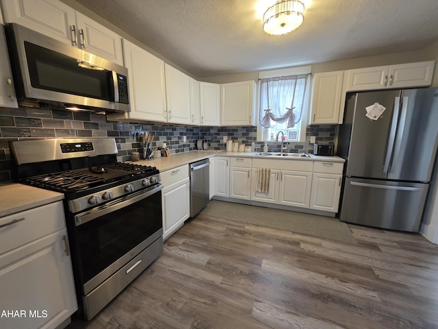 kitchen with white cabinetry, appliances with stainless steel finishes, wood finished floors, and a sink