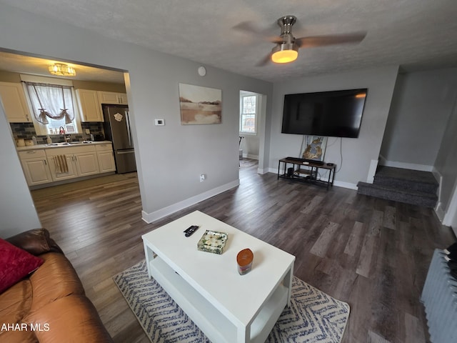 living area featuring a textured ceiling, baseboards, ceiling fan, and dark wood-style flooring