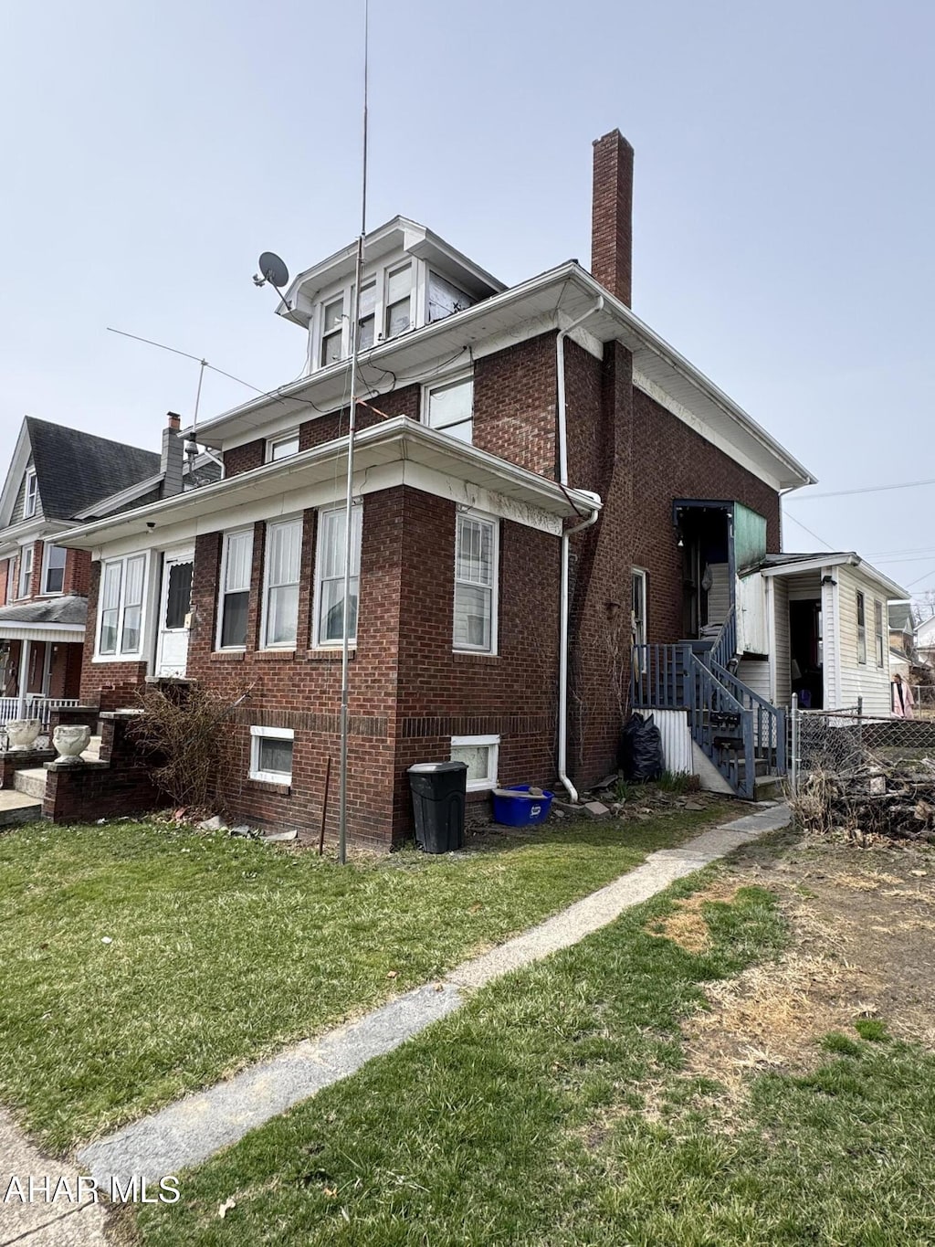 view of side of home featuring a yard, brick siding, a chimney, and fence