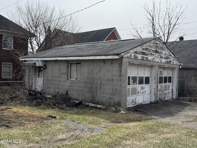 view of side of home featuring concrete block siding, an outbuilding, a detached garage, and a shingled roof
