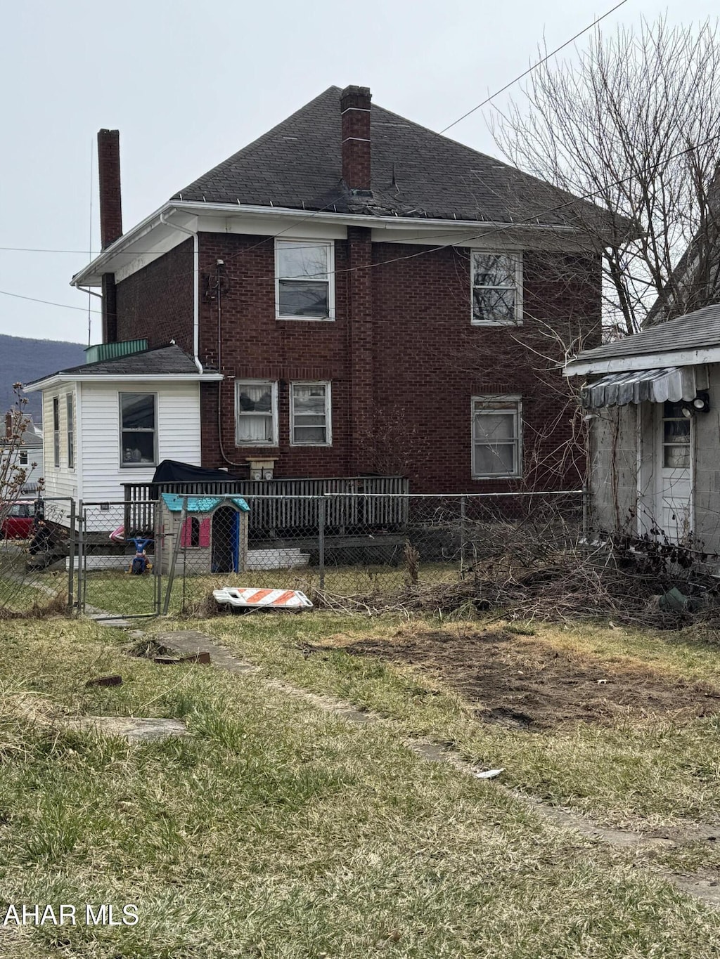 rear view of property featuring fence, brick siding, and a chimney