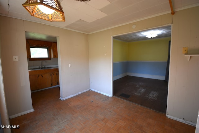 unfurnished room with baseboards, wood walls, ornamental molding, and a sink
