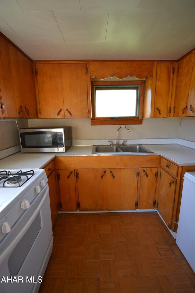 kitchen featuring brown cabinetry, gas range gas stove, a sink, light countertops, and stainless steel microwave