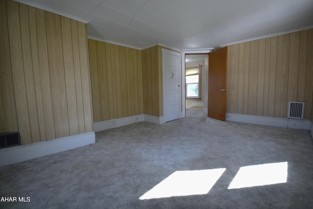 carpeted empty room featuring visible vents, wood walls, and ornamental molding