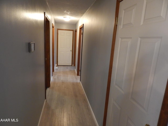 hallway with light wood-style floors, baseboards, and a textured ceiling