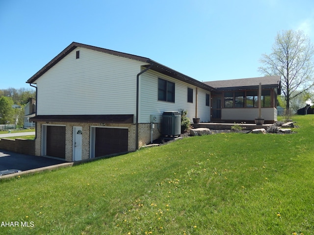 view of property exterior featuring central AC, brick siding, a garage, a sunroom, and a lawn