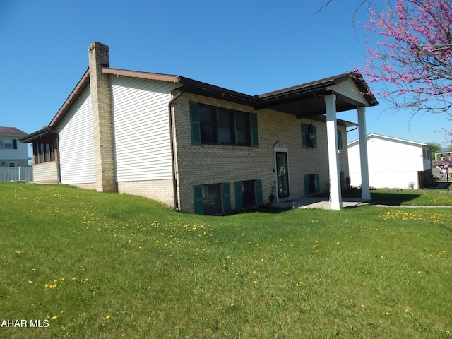 back of house with brick siding, a yard, and a chimney