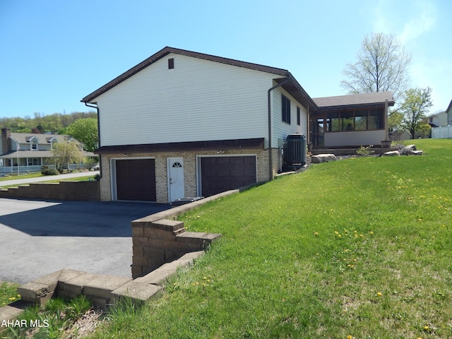 view of side of property with brick siding, a sunroom, an attached garage, central air condition unit, and driveway