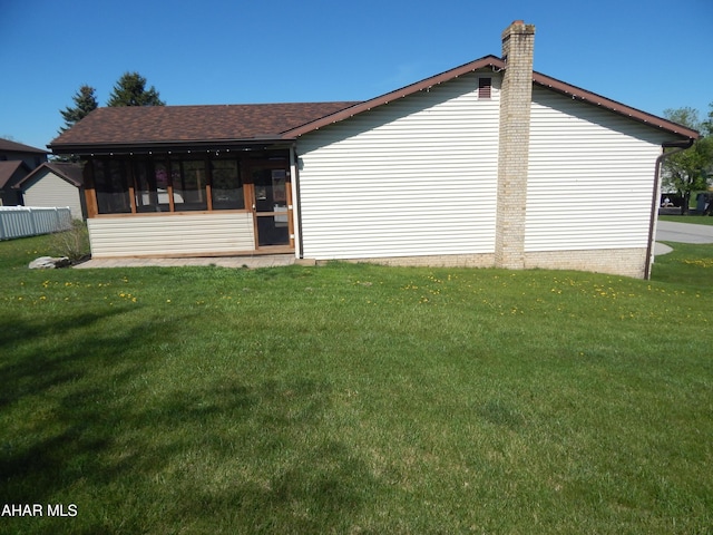 view of side of home with roof with shingles, a chimney, and a lawn