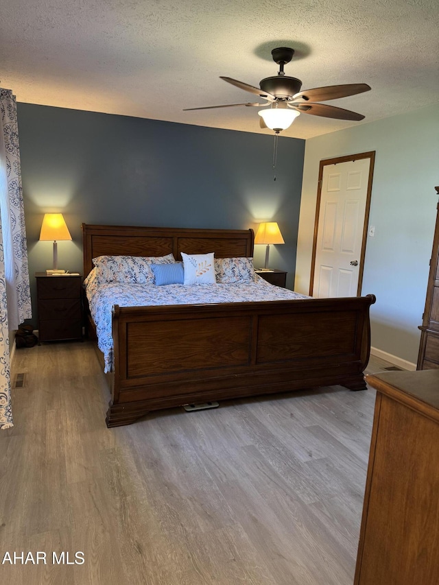 bedroom featuring a ceiling fan, a textured ceiling, visible vents, wood finished floors, and baseboards