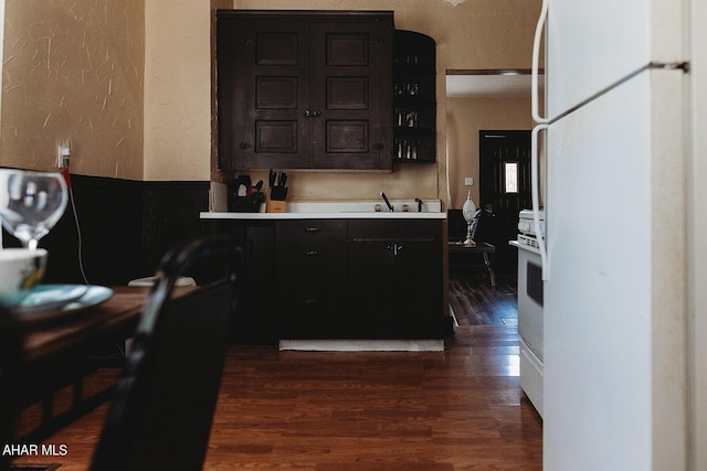 kitchen featuring dark brown cabinetry, dark hardwood / wood-style flooring, white appliances, and sink