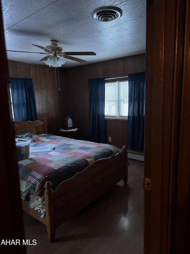 bedroom with hardwood / wood-style flooring, wooden walls, a baseboard radiator, and ceiling fan