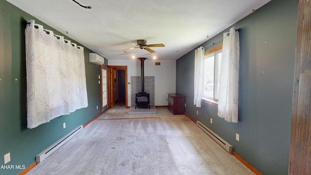 unfurnished living room with baseboard heating, a wood stove, light colored carpet, and an AC wall unit