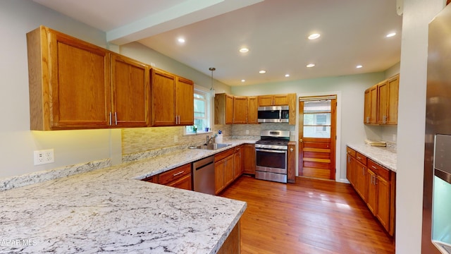 kitchen featuring pendant lighting, hardwood / wood-style floors, sink, appliances with stainless steel finishes, and tasteful backsplash