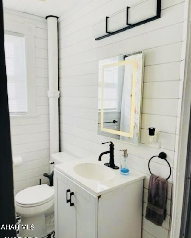 bathroom with wood walls, plenty of natural light, vanity, and toilet