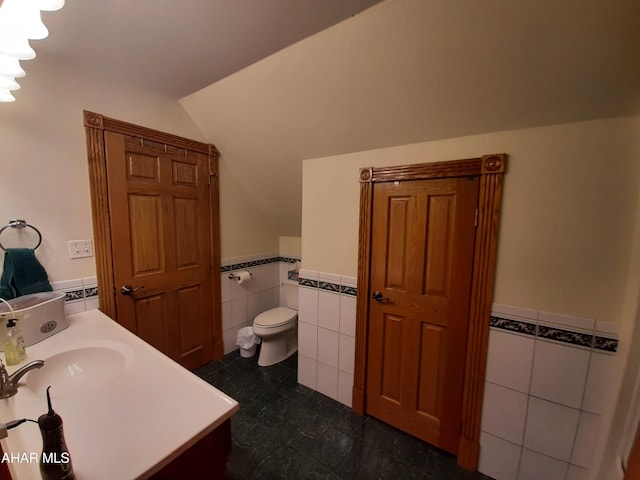 bathroom with tile patterned floors, vaulted ceiling, toilet, vanity, and tile walls