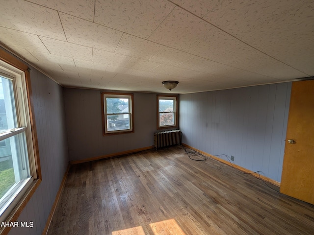 unfurnished room with hardwood / wood-style floors, radiator, and wood walls