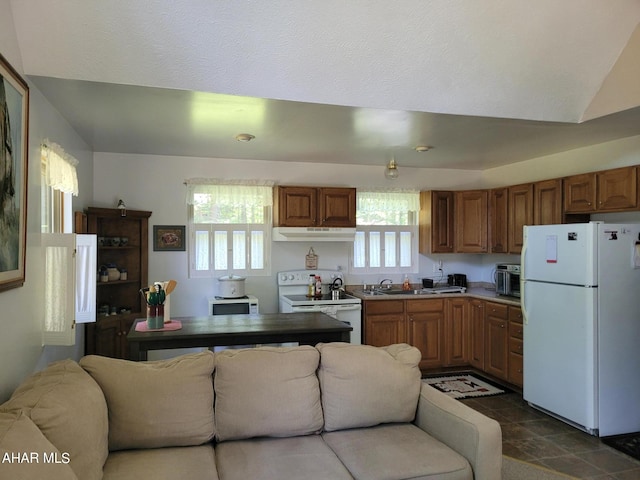 kitchen with white appliances, under cabinet range hood, open floor plan, and brown cabinetry