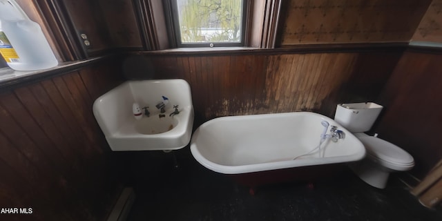 bathroom featuring a washtub, toilet, and wooden walls