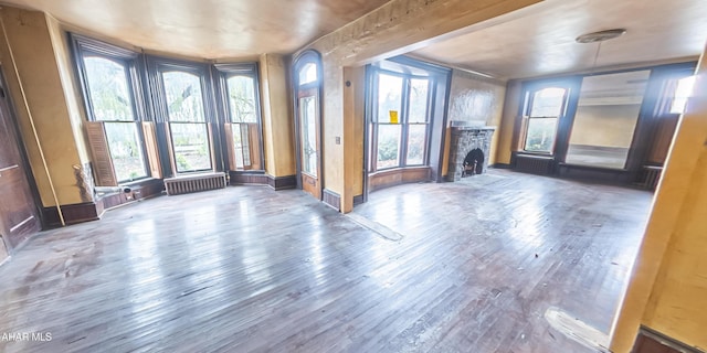 unfurnished living room with hardwood / wood-style flooring, radiator heating unit, and a fireplace