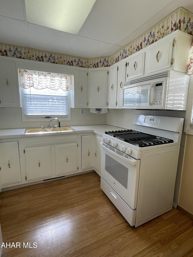 kitchen featuring sink, white appliances, a paneled ceiling, white cabinets, and light wood-type flooring