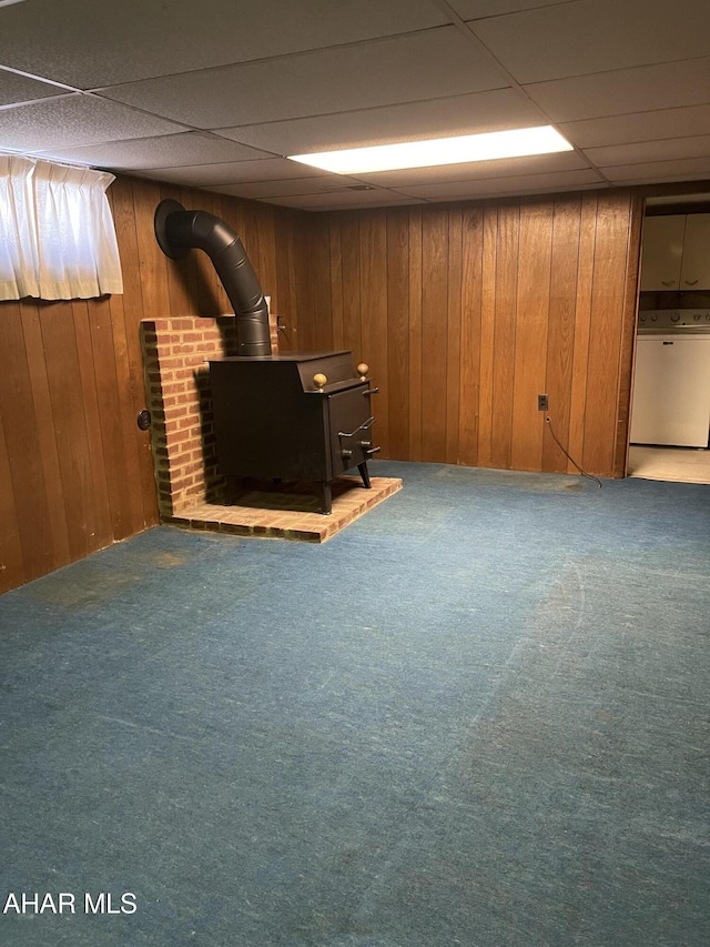 basement featuring wooden walls, carpet floors, a drop ceiling, washer / dryer, and a wood stove