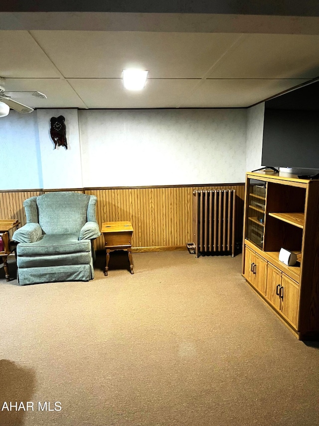 living room featuring ceiling fan, radiator, wooden walls, and light colored carpet