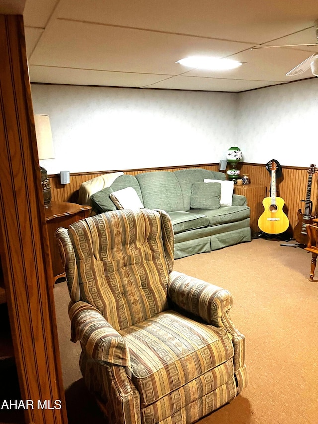 living area with carpet, a paneled ceiling, and wooden walls