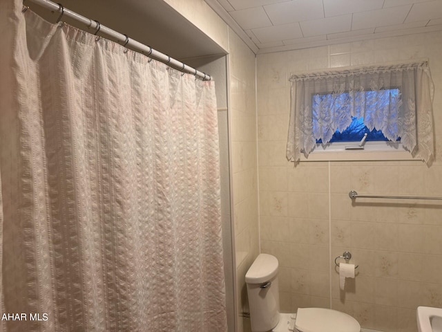 bathroom featuring a shower with shower curtain, tile walls, and toilet