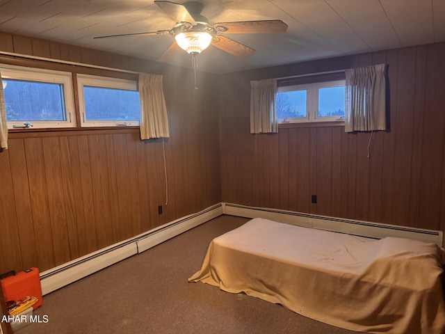 unfurnished bedroom with carpet flooring, ceiling fan, wooden walls, and a baseboard radiator