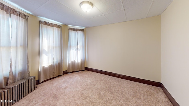 carpeted spare room featuring baseboards, a paneled ceiling, and radiator heating unit