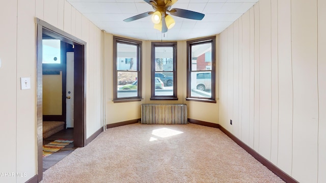 spare room featuring baseboards, light colored carpet, ceiling fan, and radiator heating unit