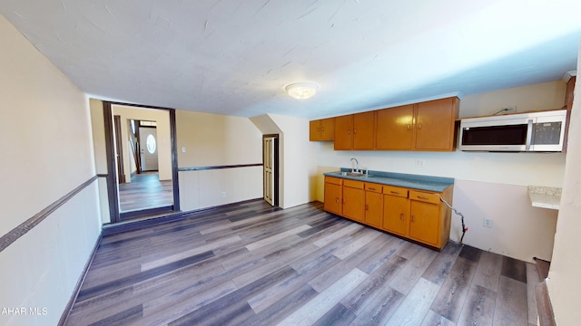 kitchen featuring stainless steel microwave, brown cabinets, a sink, and wood finished floors