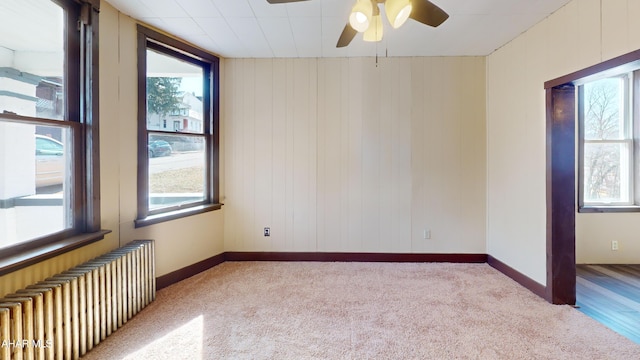 unfurnished room featuring baseboards, radiator, a ceiling fan, and carpet