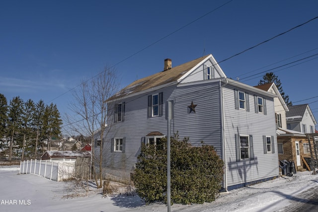 view of snowy exterior with fence and a chimney