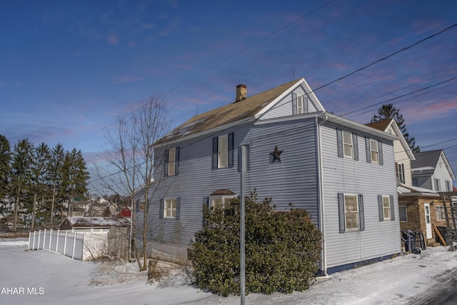 view of snow covered exterior featuring a chimney and fence