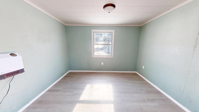 spare room featuring heating unit, a textured wall, ornamental molding, light wood-type flooring, and baseboards