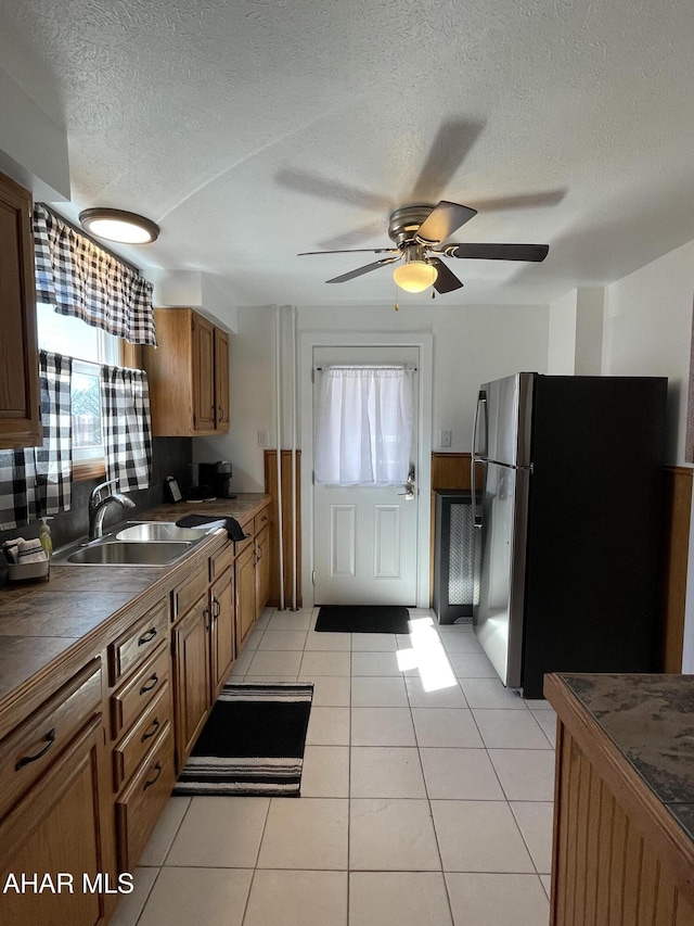 kitchen featuring light tile patterned floors, brown cabinets, freestanding refrigerator, and a sink